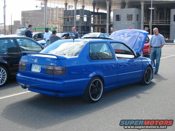 Blue Volkswagen Jetta modified into a pickup truck, seen from the rear quarter. It has a custom bed and spoiler