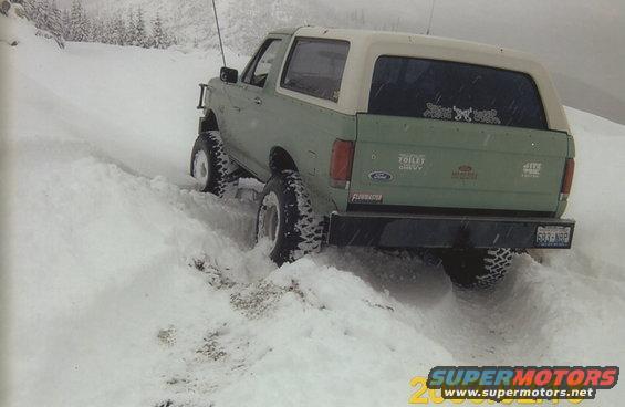 Green Ford Bronco with a white top driving in snow, rear view