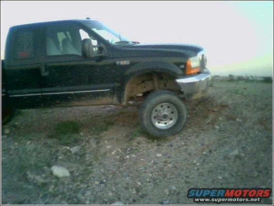 Black 1999 Ford F-250 truck parked on a gravelly surface with a distant landscape