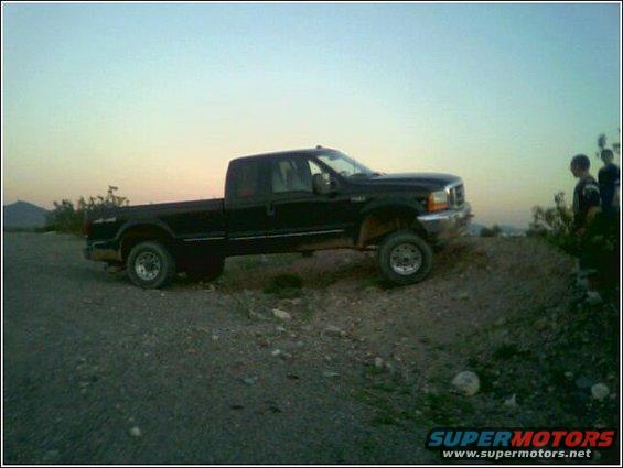Black 1999 Ford F-250 pickup truck parked on a dirt incline with two people standing to the right