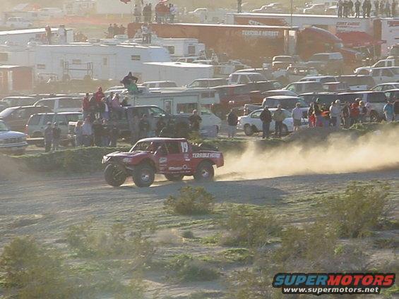 Red off-road truck with number 19, kicking up dust on a dirt track