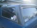 1981 Ford Bronco - A blue pickup truck with a camper shell is parked in front of a garage. Stickers adorn the rear window.