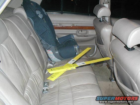Car interior with tan leather seats, a child car seat, and two yellow windshield wiper packages on the back seat