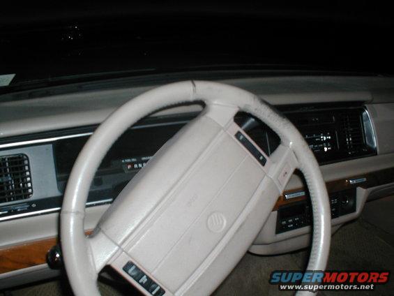 Car interior with a light-colored steering wheel and dashboard. Wood trim accents are visible