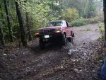Red 1992 Ford F-150 pickup truck driving on a muddy forest road