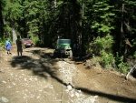 Green Jeep on a dirt road with two people walking