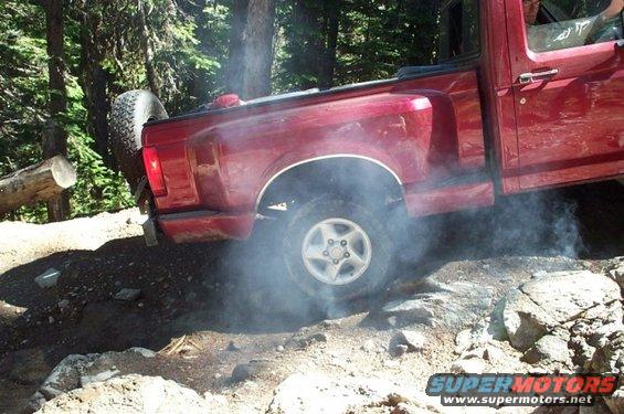 Red 1992 Ford F-150 kicking up dust and smoke while driving over rocks