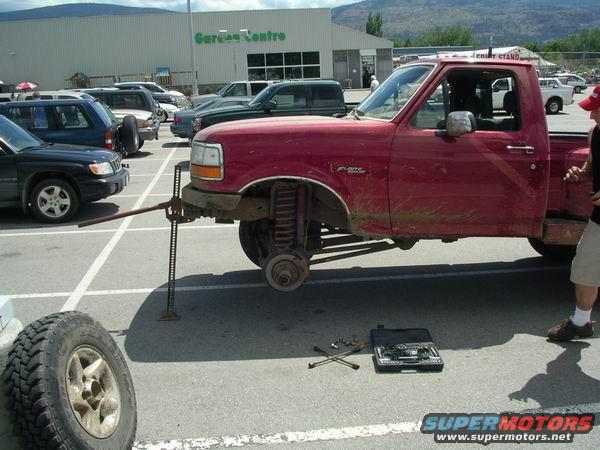 red pickup truck jacked up, front wheel off, tools on ground
