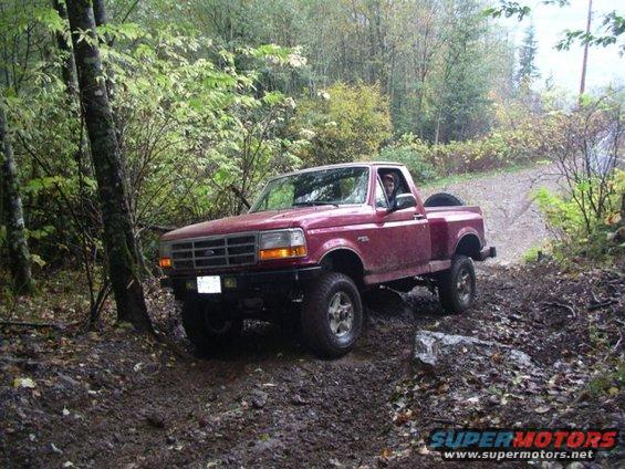 1992 Ford F-150 pickup truck driving on a muddy trail with trees on the side