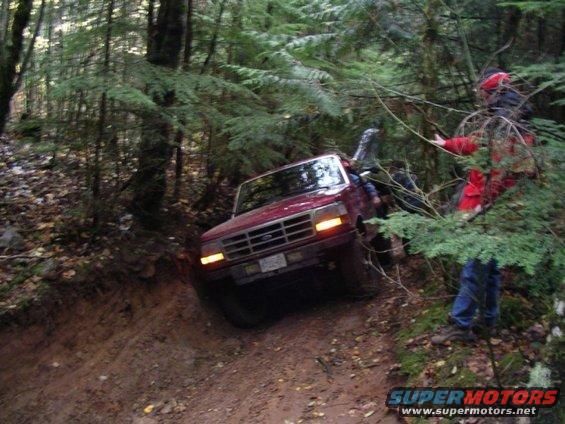 Red 1992 Ford F-150 driving off-road on a steep, muddy incline with trees on either side
