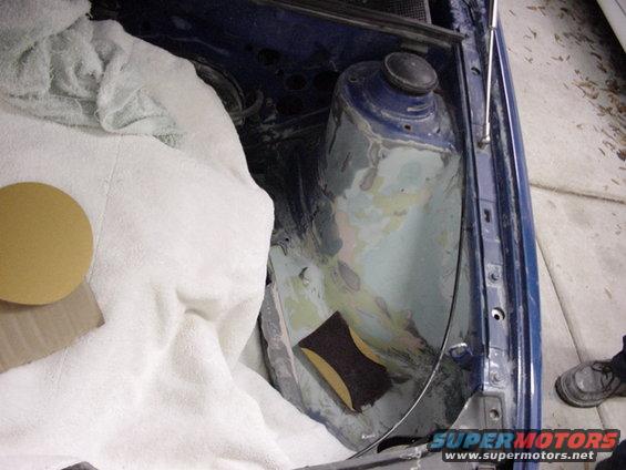 Blue car's engine bay with body filler and sanding block. White towel covers part of the area