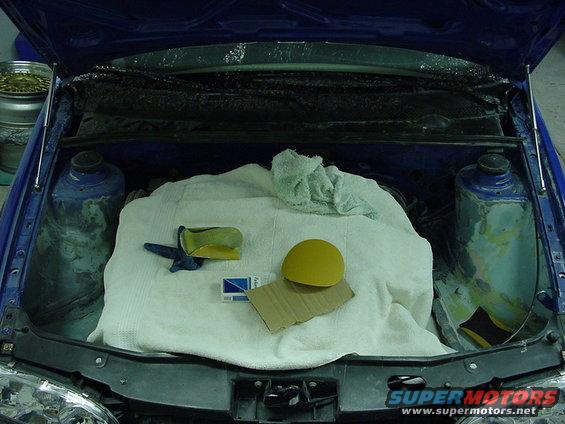 Open car hood showing engine bay with a white cloth covering parts, a yellow sanding pad, and a blue glove