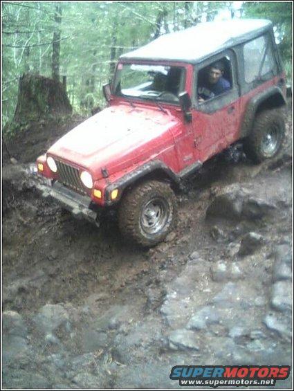 Red Jeep TJ navigating a muddy, rocky trail in a forest