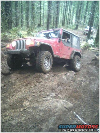 Red Jeep Wrangler on a dirt trail in a forest, with another vehicle behind it