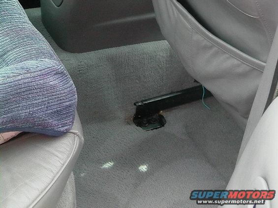 Car interior floor showing gray carpet, seat rails, and part of a seat cushion