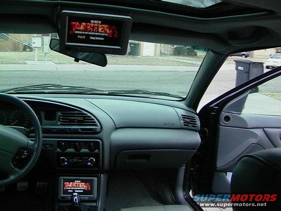 car interior showing dashboard, steering wheel, and two screens displaying media