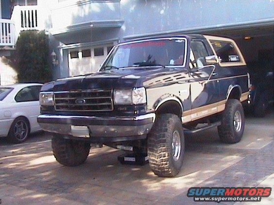 Lifted dark blue and tan Ford Bronco parked in a driveway, front end visible