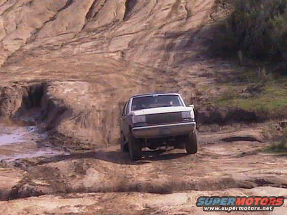 White SUV driving up a dirt hill, front view. The vehicle has a dark grille and appears to be from the late 1980s