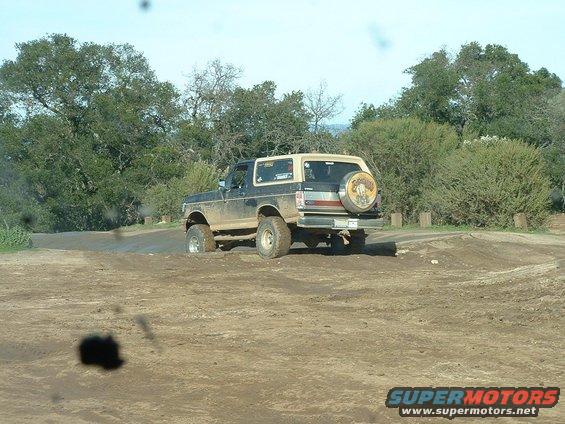 1991 Ford Bronco driving on a dirt track with trees in the background