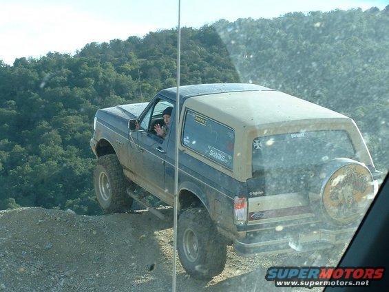 Dark blue and tan Ford Bronco with off-road tires driving on a dirt hill