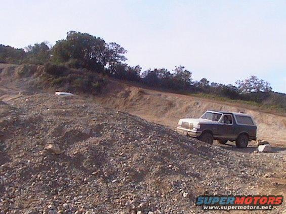 1991 Ford Bronco driving up a rocky incline on a sunny day