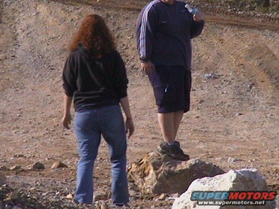 Two people stand in a dirt area, one holding a water bottle