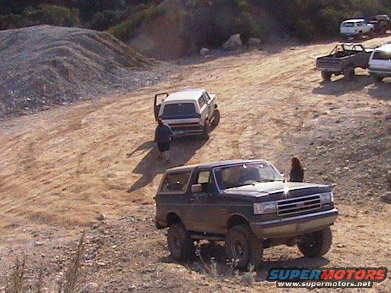 1991 Ford Bronco parked on a dirt hill with other vehicles in the background
