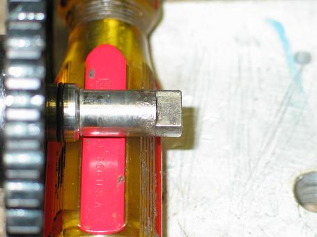 Close-up of a metal shaft extending from a red and yellow tool, with a gear to the left