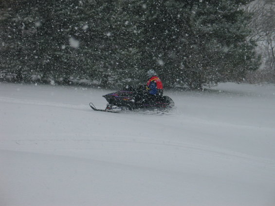 Snowmobile with rider in colorful jacket moving through falling snow