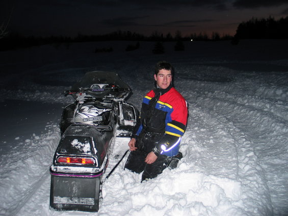 Snowmobile in snow with a person kneeling beside it