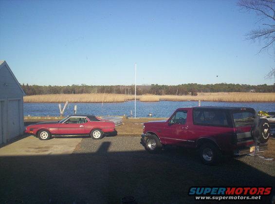 Red 1971 Ford Mustang coupe and red Ford Bronco parked by a body of water