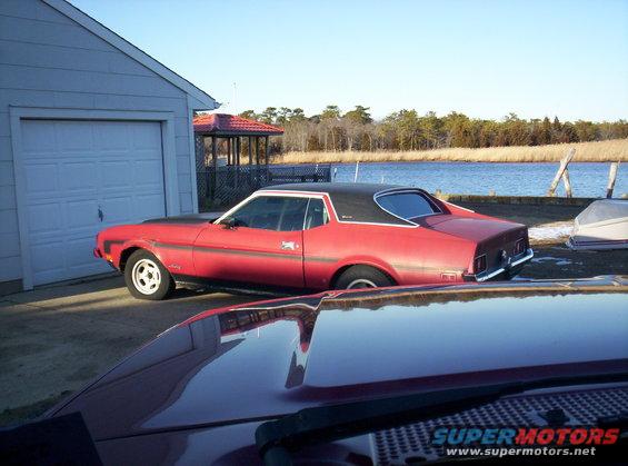 Red 1971 Ford Mustang coupe with a black vinyl roof parked next to a garage