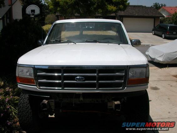 White Ford Bronco front end with chrome grille and orange turn signals. Tires and bumper visible