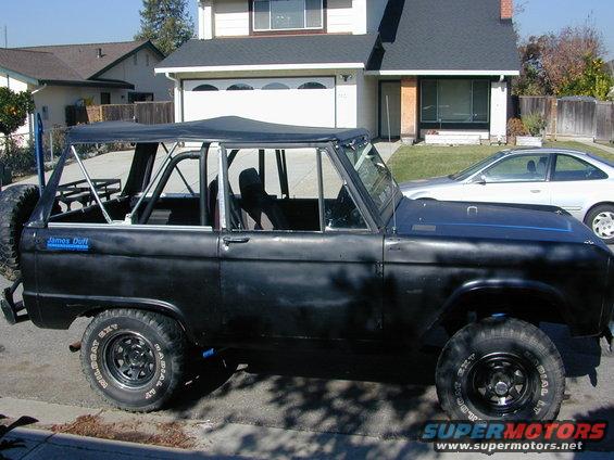1967 Ford Bronco, black with roll cage, soft top, and spare tire on rear. James Duff sticker on fender