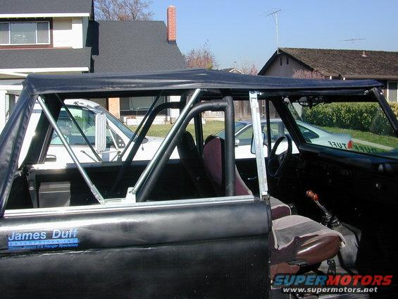Black Ford Bronco interior with roll cage, brown seats, and a "James Duff Enterprises" sticker