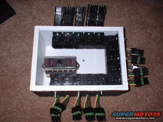 Automotive fuse box with multiple relays and wiring harnesses, viewed from above