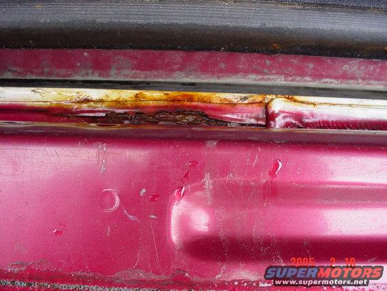 Close-up of rusted door frame on a red vehicle, with a black rubber seal above