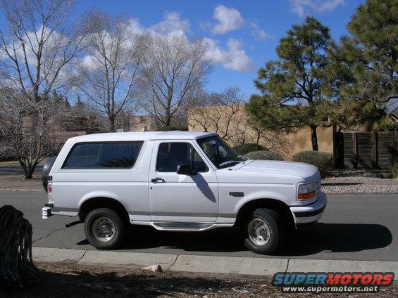 White Ford Bronco parked on street, side view. Spare tire visible on rear