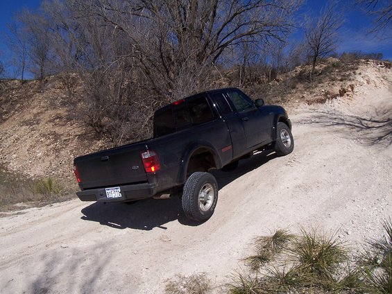 Black 2003 Ford Ranger pickup truck driving on a dirt road with sparse trees and blue sky