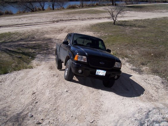 Black Ford Ranger pickup truck driving up a dirt hill near a body of water