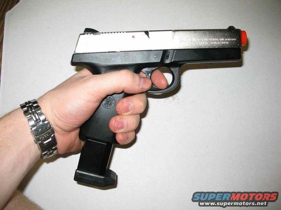 hand with watch holding a pistol with orange tip and extended magazine