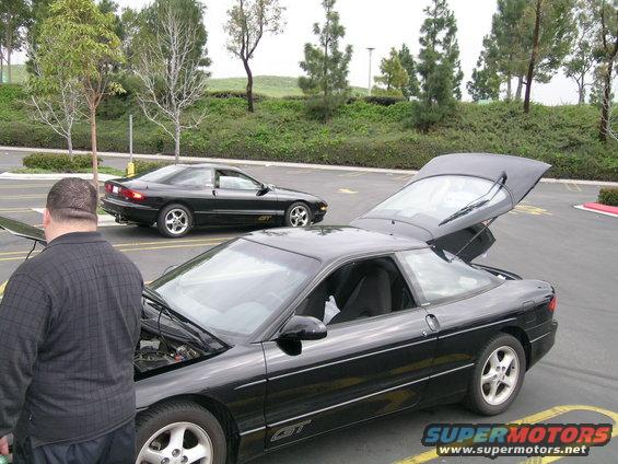 Two black Ford Probes parked in a lot, one with hood open and trunk up