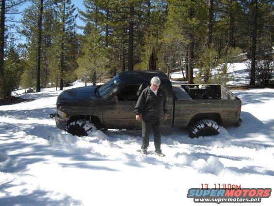 Side view of a dark pickup truck stuck in deep snow, with a person standing beside it