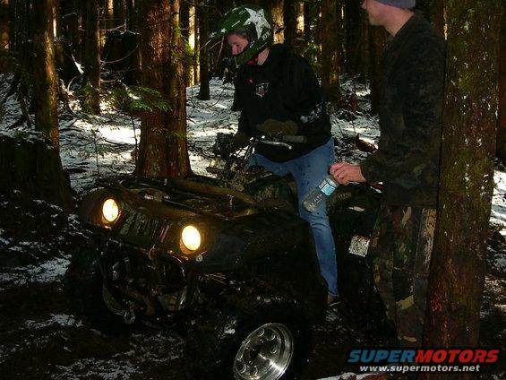All-terrain vehicle stuck in mud with two people nearby