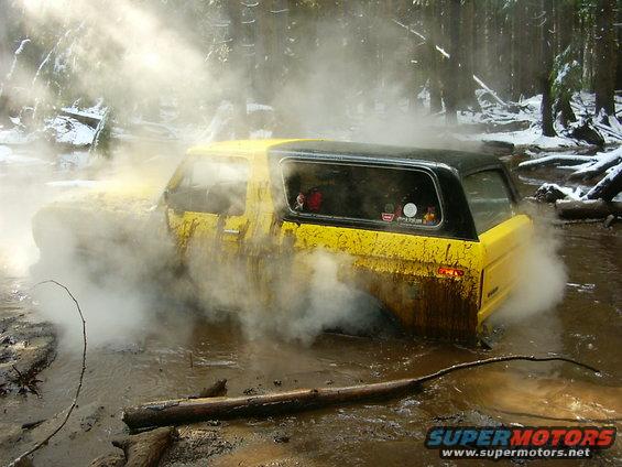 Yellow SUV stuck in muddy water with steam rising