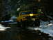 1990 Ford Bronco - A lifted yellow Ford Bronco navigates a wet and snowy forest path.