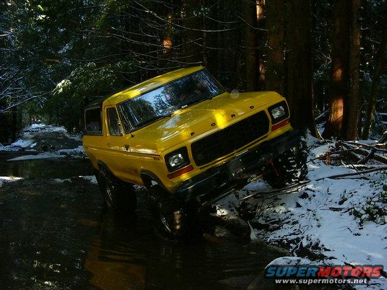 Yellow 1978 Ford Bronco driving through water and snow in a forest