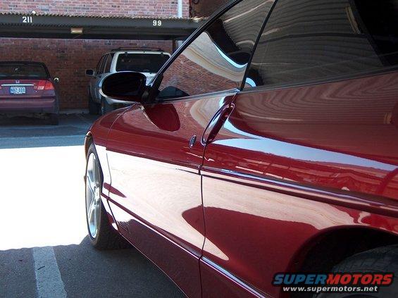 Red 1996 Ford Probe side door and fender detail. Other cars parked in background