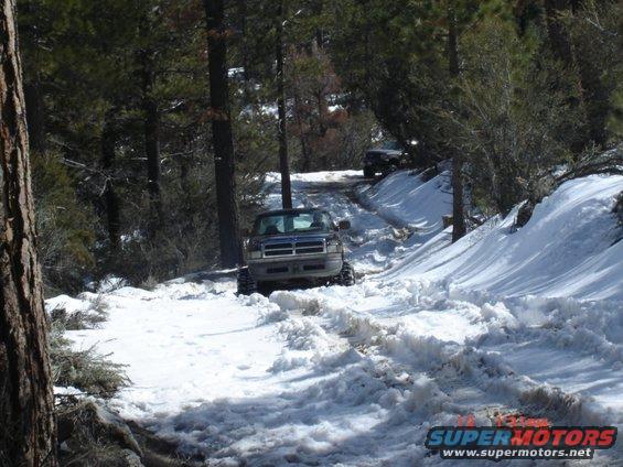 Dark blue Ford F-Series truck with large tires driving on a snow-covered road