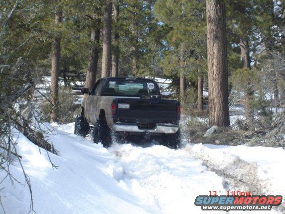 Truck with large tires driving through snow, rear view